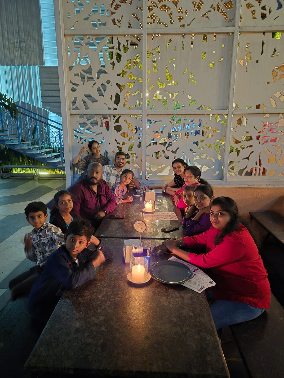 A group of adults and children seated along a long table with lit candles, looking at the camera.